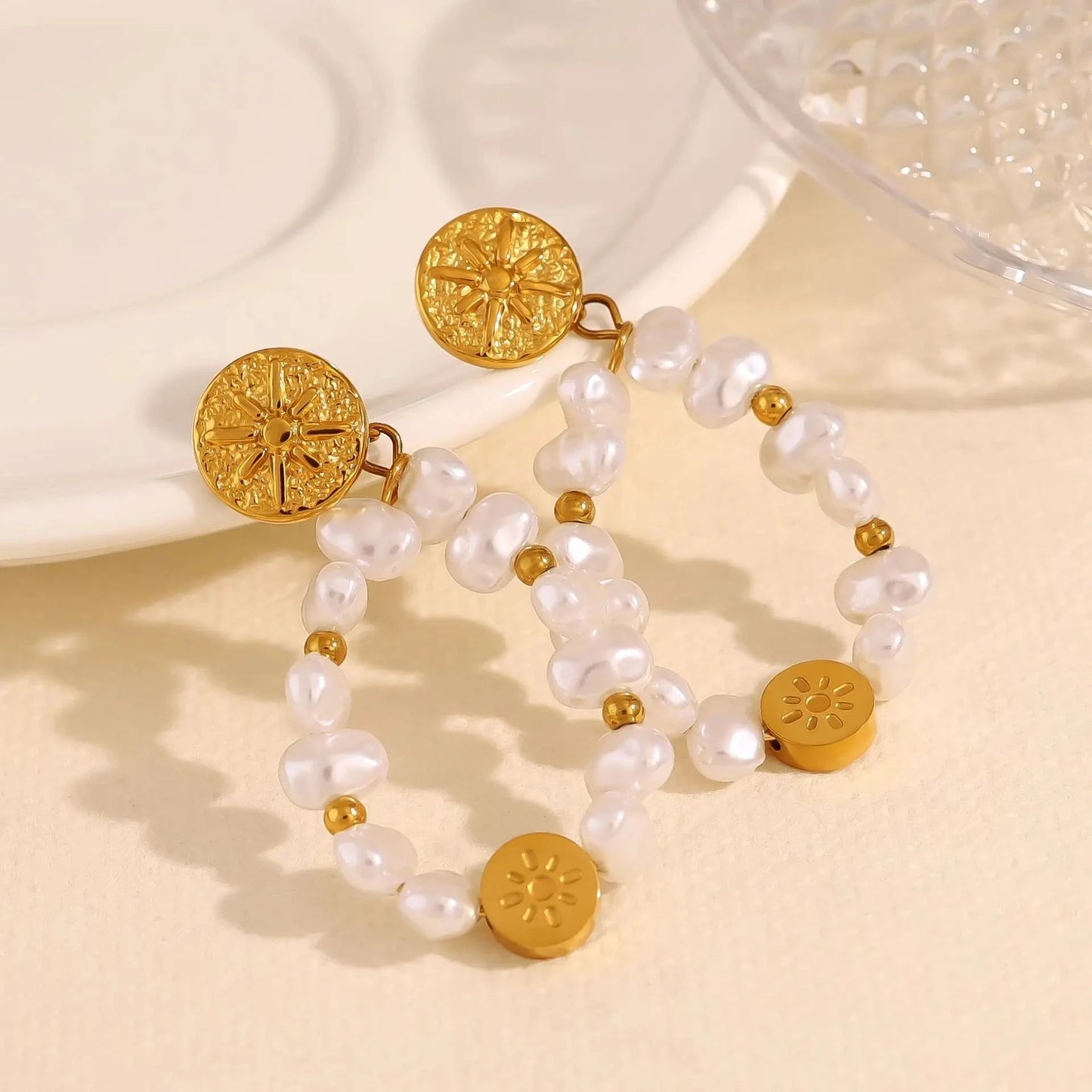 Pair of gold and pearl earrings on a beige surface