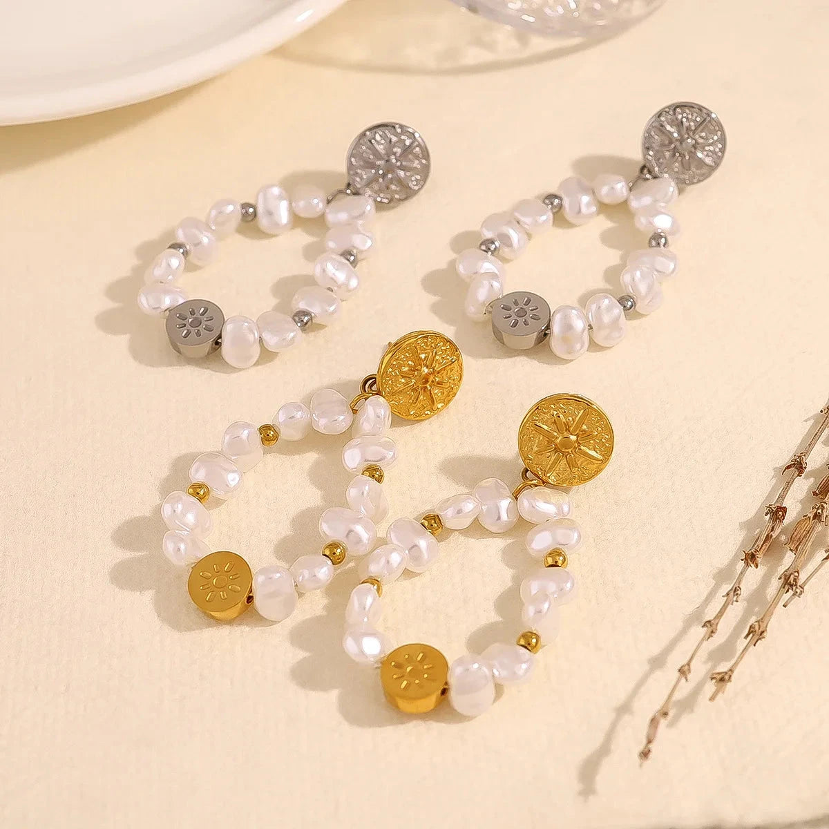 Two pair of pearl earrings with gold and silver accents on a beige surface