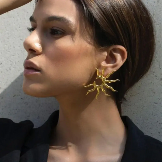 Woman wearing gold sun-shaped earrings against a neutral background