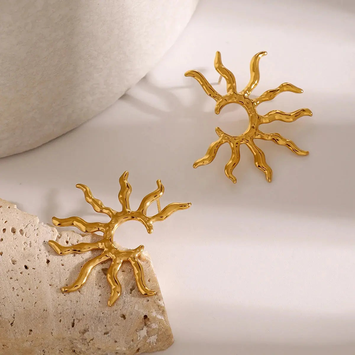 Gold sun-shaped fashion earrings on a textured surface. Waterproof, tarnish-free, hypoallergenic