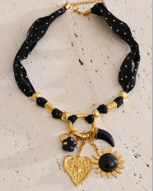 Black beaded necklace with gold accents and charms on a textured surface