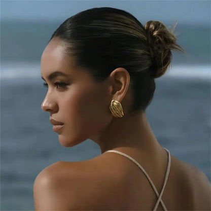Woman with a bun and gold earring against a blurred ocean background