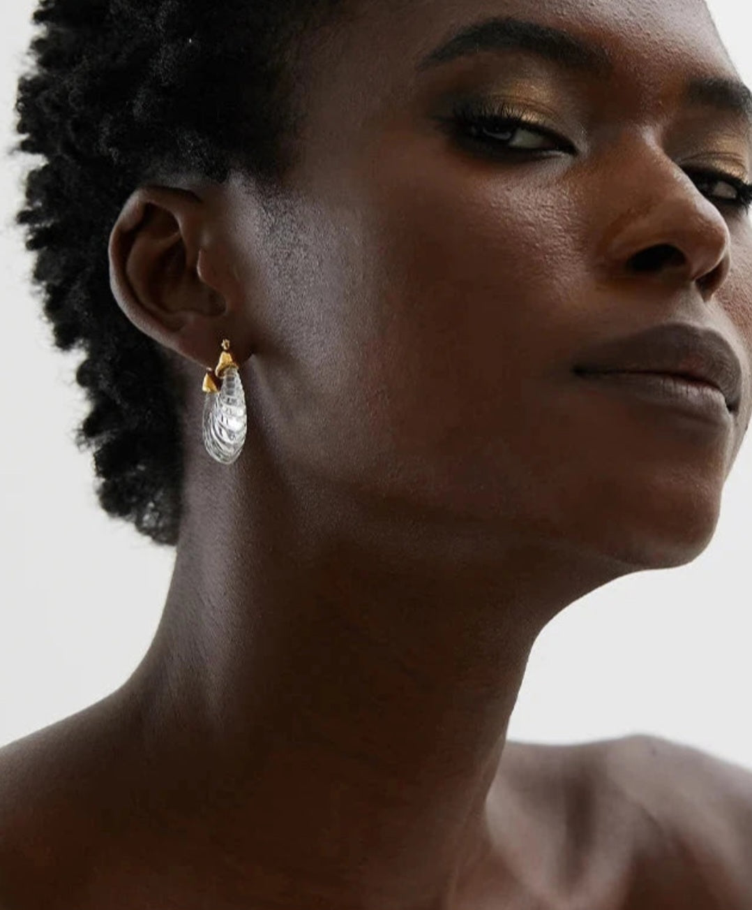 Close-up of a woman wearing a gold earring with a clear gemstone on a neutral background