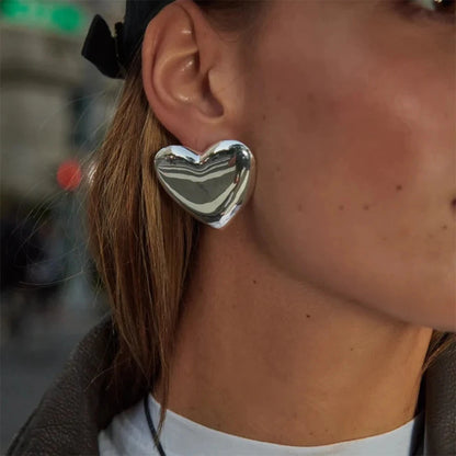 Close-up of a person wearing a silver stainless steel  heart-shaped earring with a blurred background.