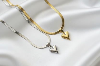 Two heart-shaped pendants on gold and silver necklaces against a white satin background