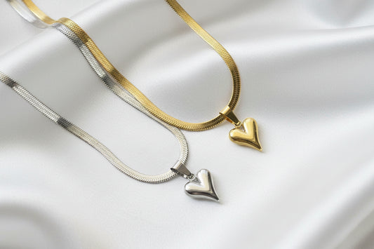 Two heart-shaped pendants on gold and silver necklaces against a white satin background