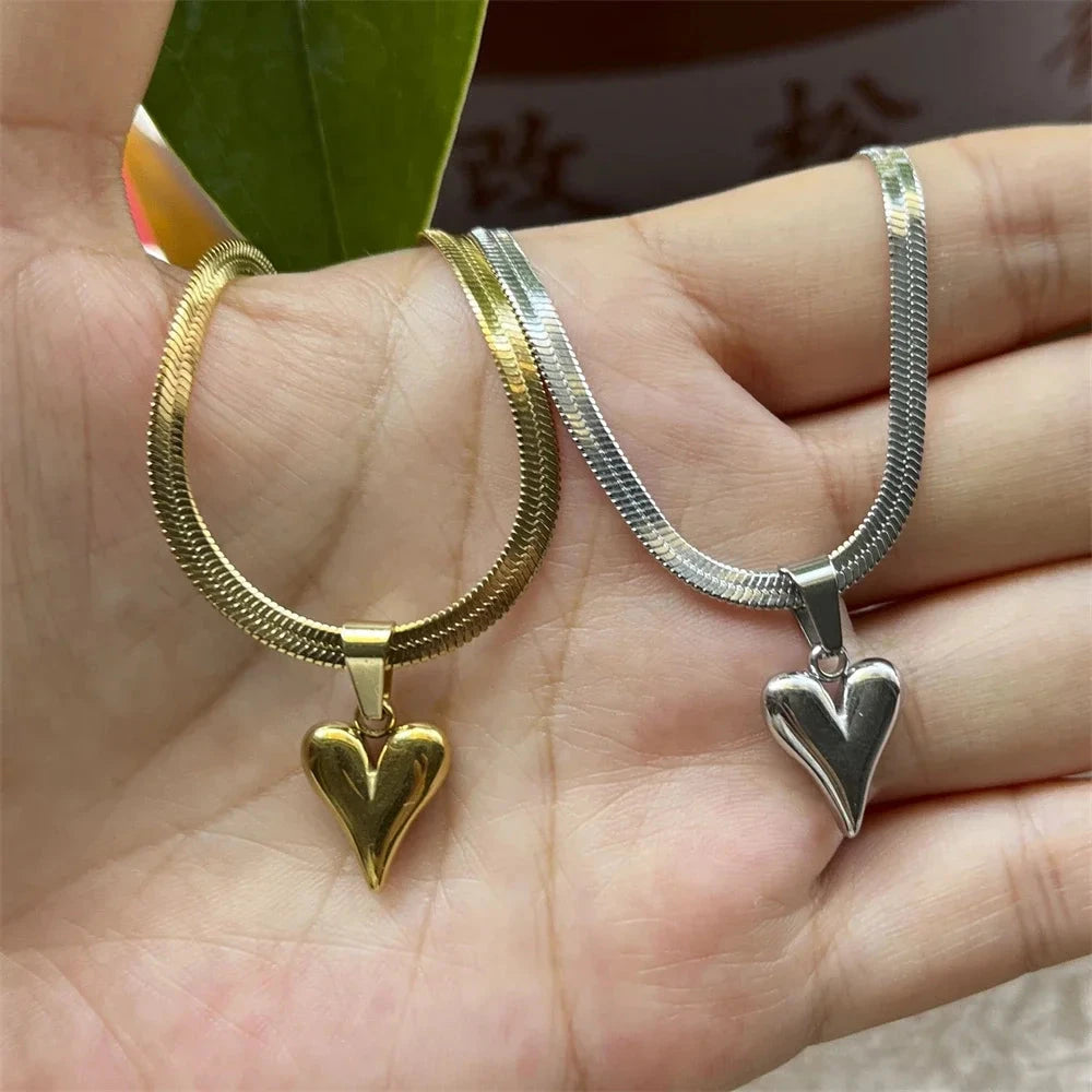 Gold and silver heart-shaped pendants on snake chain necklaces held in a hand.