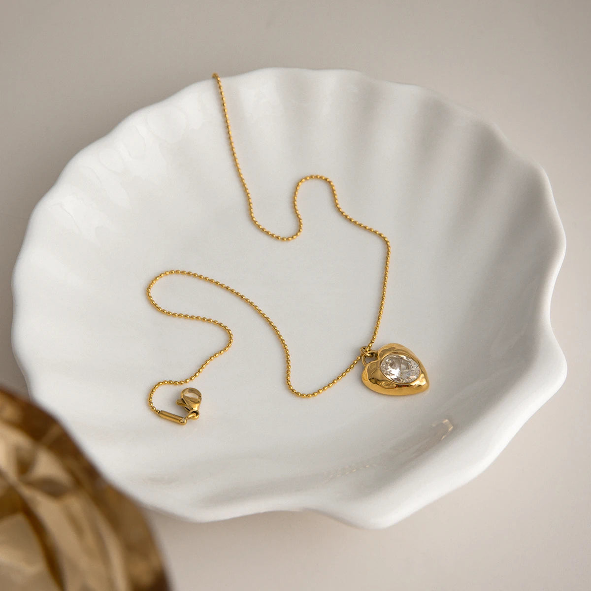 18k gold-plated necklace with a heart-shaped pendant on a white shell dish.
