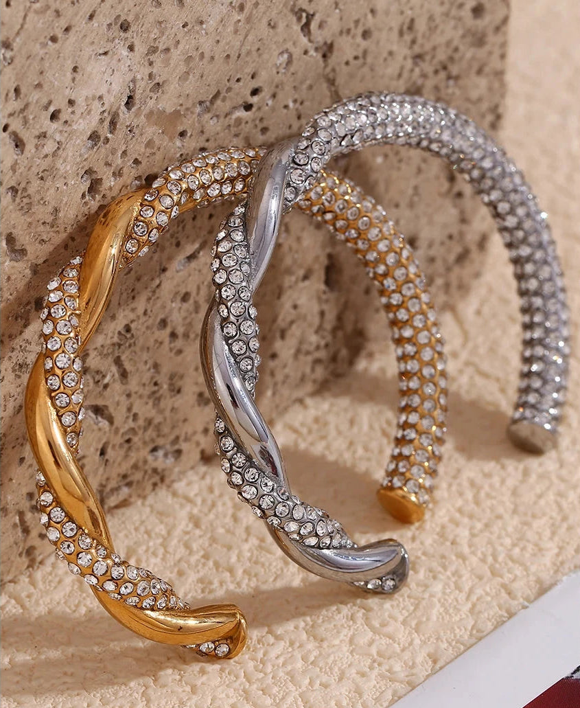 Two gold and silver bracelets with diamond-like stones on a textured beige surface.