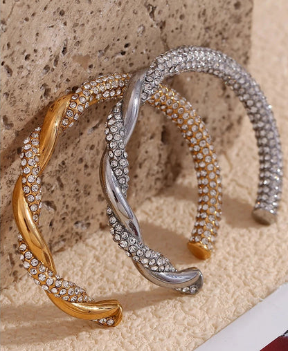 Two gold and silver bracelets with diamond-like stones on a textured beige surface.
