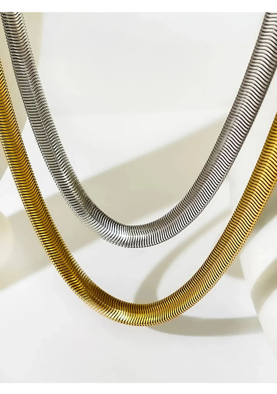 Two necklaces, one gold and one silver, on a light background