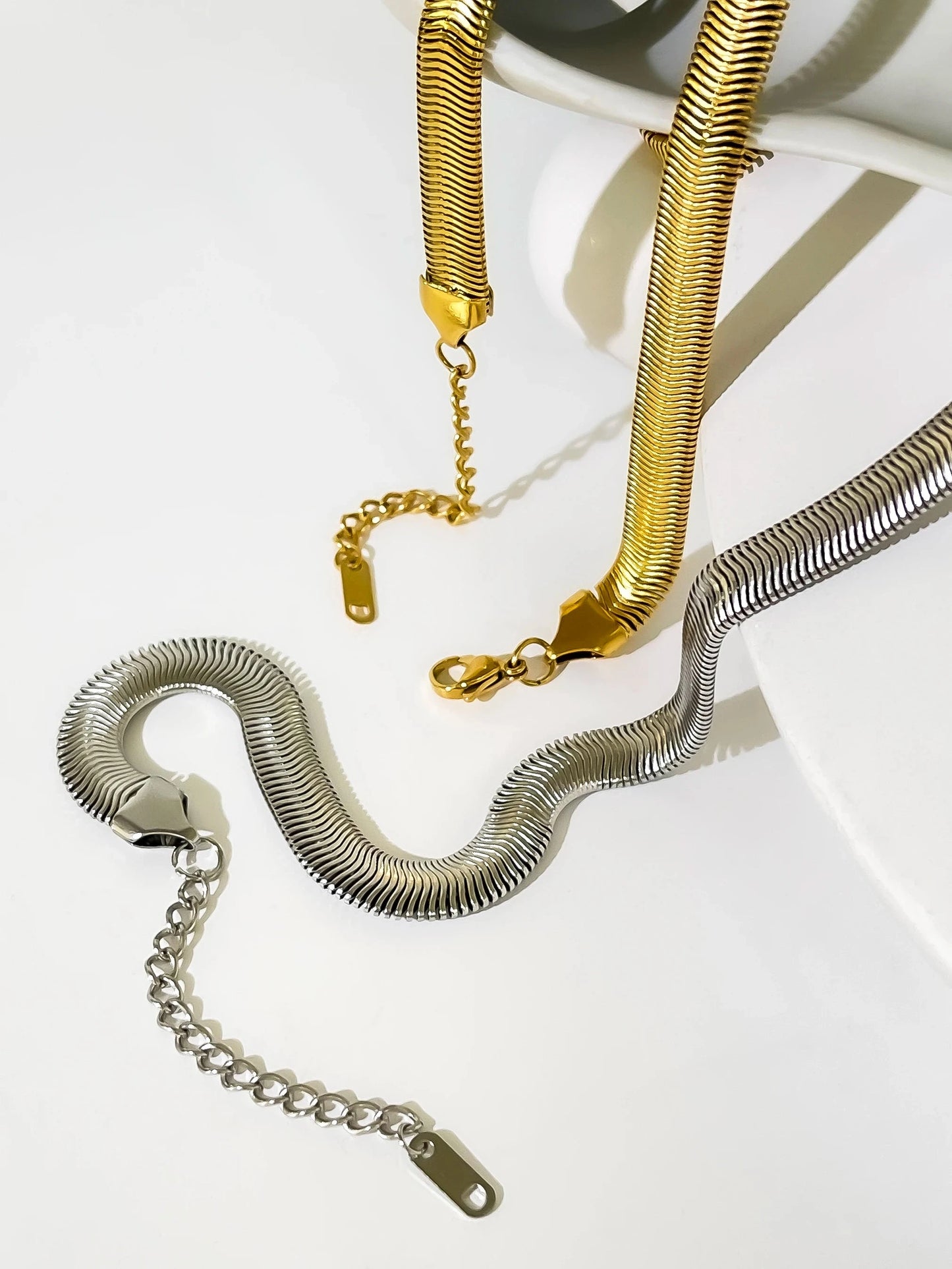 Gold and silver snake chain necklaces on a white surface