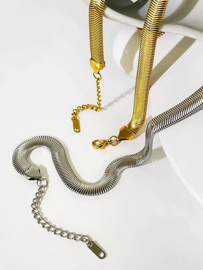 Gold and silver snake chain necklaces on a white surface