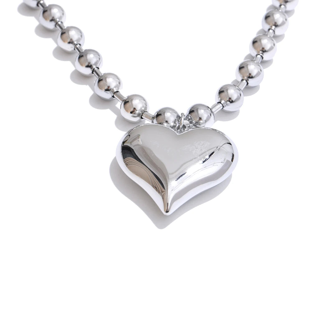 Silver heart-shaped pendant on a beaded chain Close-up of silver Chunky Heart Necklace texture and gold-plated finish over stainless steel.