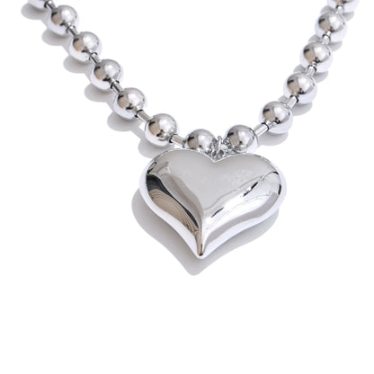 Silver heart-shaped pendant on a beaded chain Close-up of silver Chunky Heart Necklace texture and gold-plated finish over stainless steel.