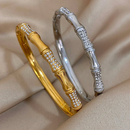 Gold and silver bamboo-style bracelets with cubic zirconias on a beige fabric background