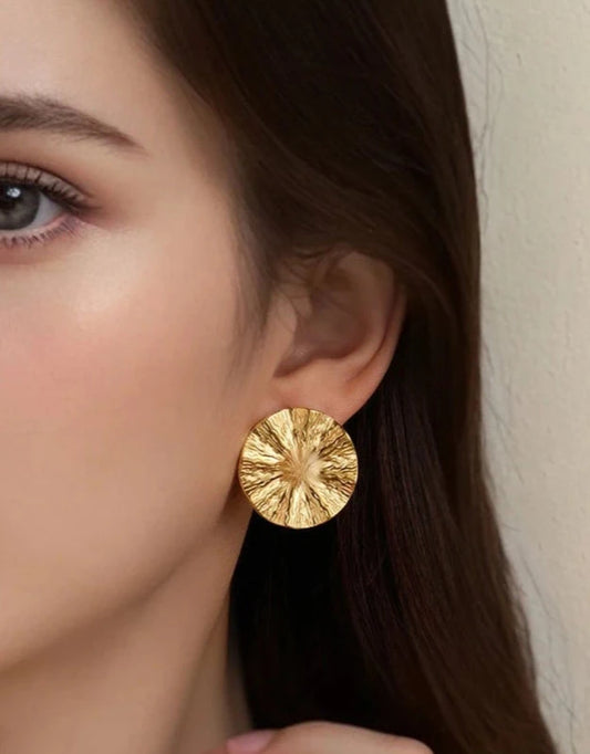 Close-up of a person wearing a gold earring with a textured design Rebecca Bloom