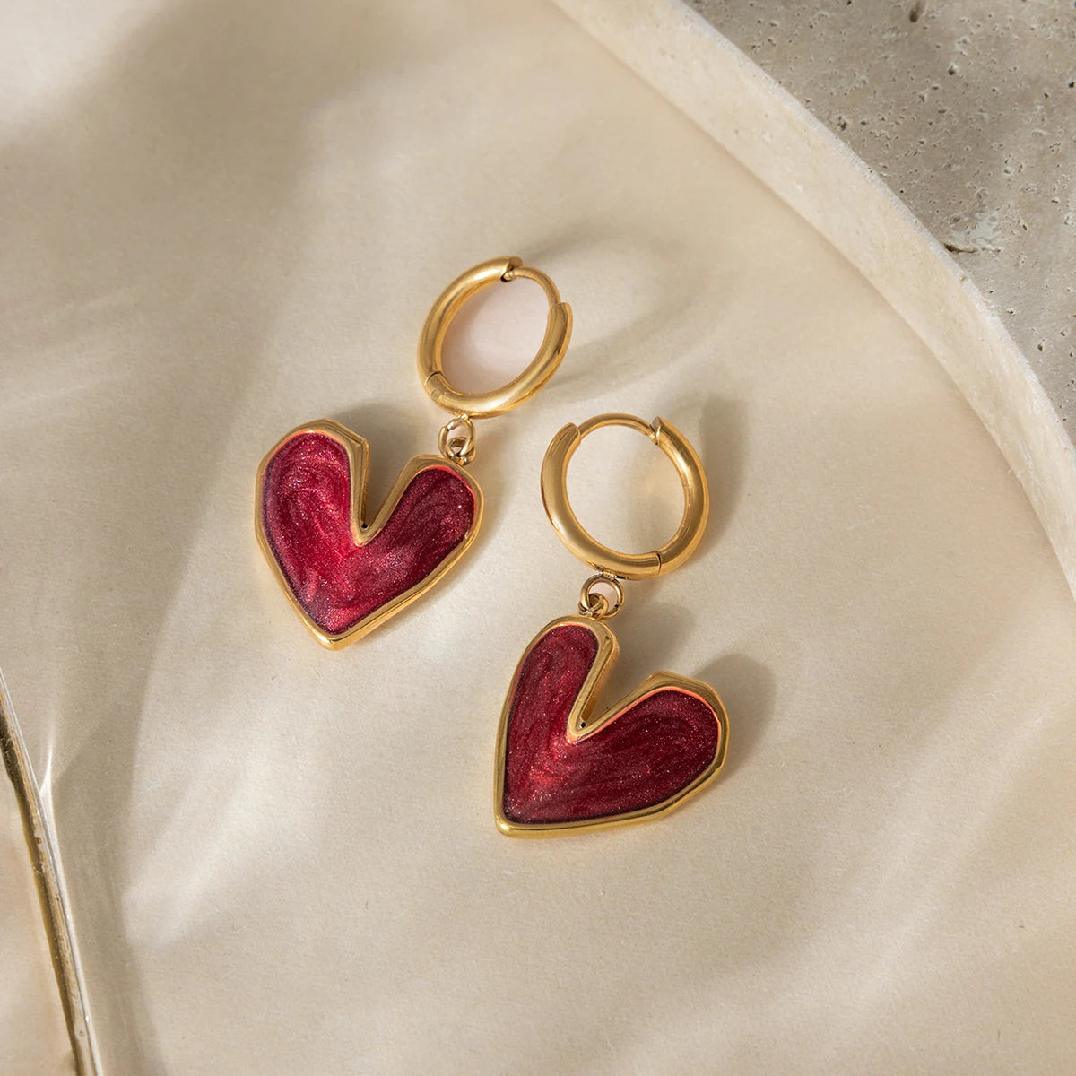 Heart-shaped earrings with 18K gold-plated frames on a beige surface