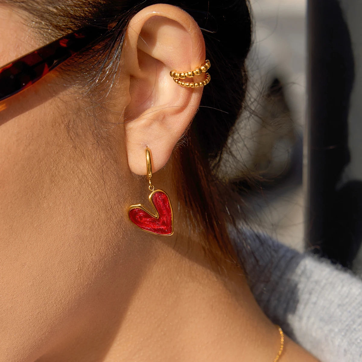 Close-up of an ear wearing an 18K gold-plated earring with a red heart design.