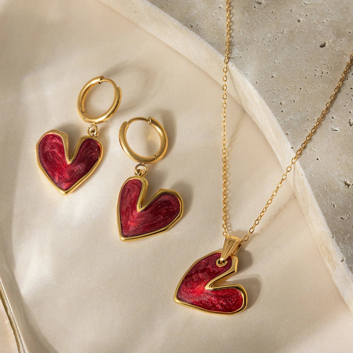 Heart-shaped jewelry set with gold and red heart earrings and pendant on a neutral background