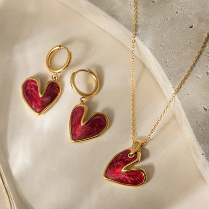 Heart-shaped jewelry set with gold and red heart earrings and pendant on a neutral background