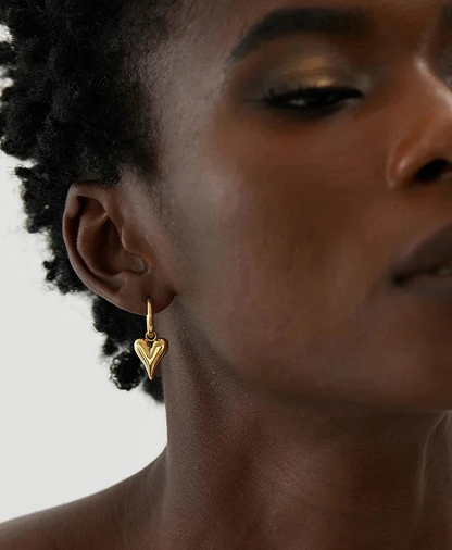 Huggie Heart Earrings Woman wearing small, gold-tone heart huggie hoop earrings, styled for a modern, elegant look.