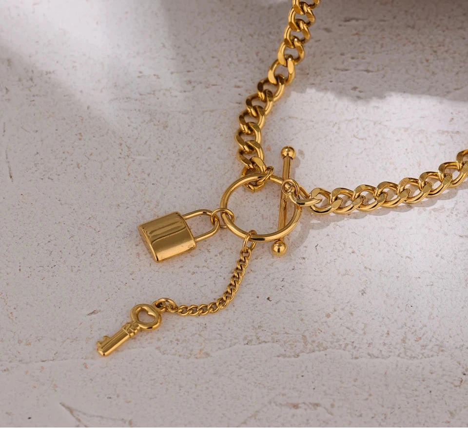 Gold chain necklace with a lock and key charm on a light gray background