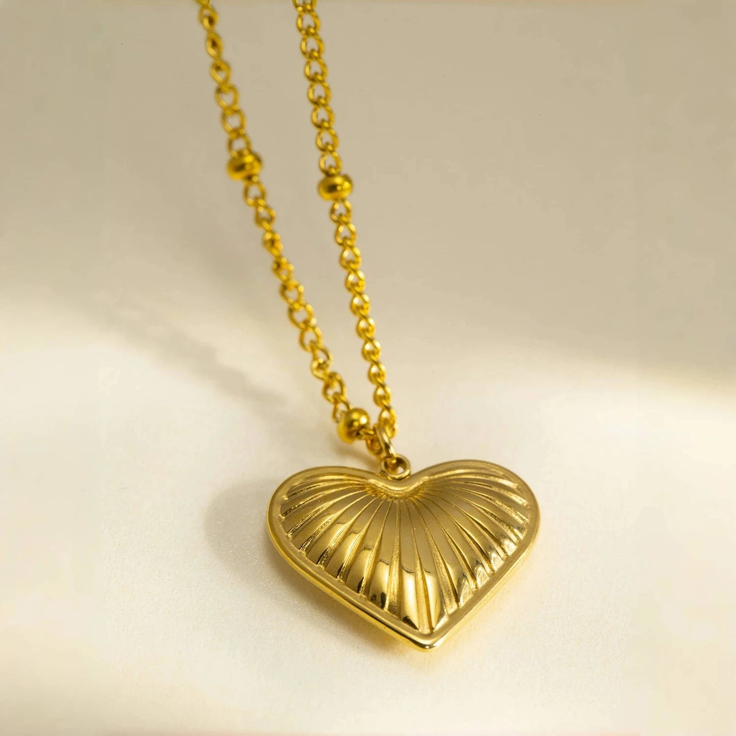 Gold heart-shaped pendant necklace on a beige background