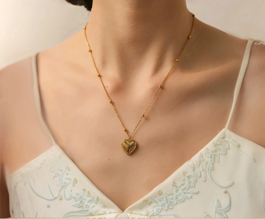 Gold necklace with a heart pendant worn by a model in a white lace top.
