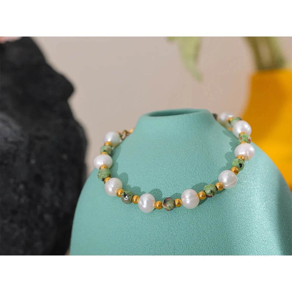 stainless steel pearl bracelet on a turquoise stand with a blurred background