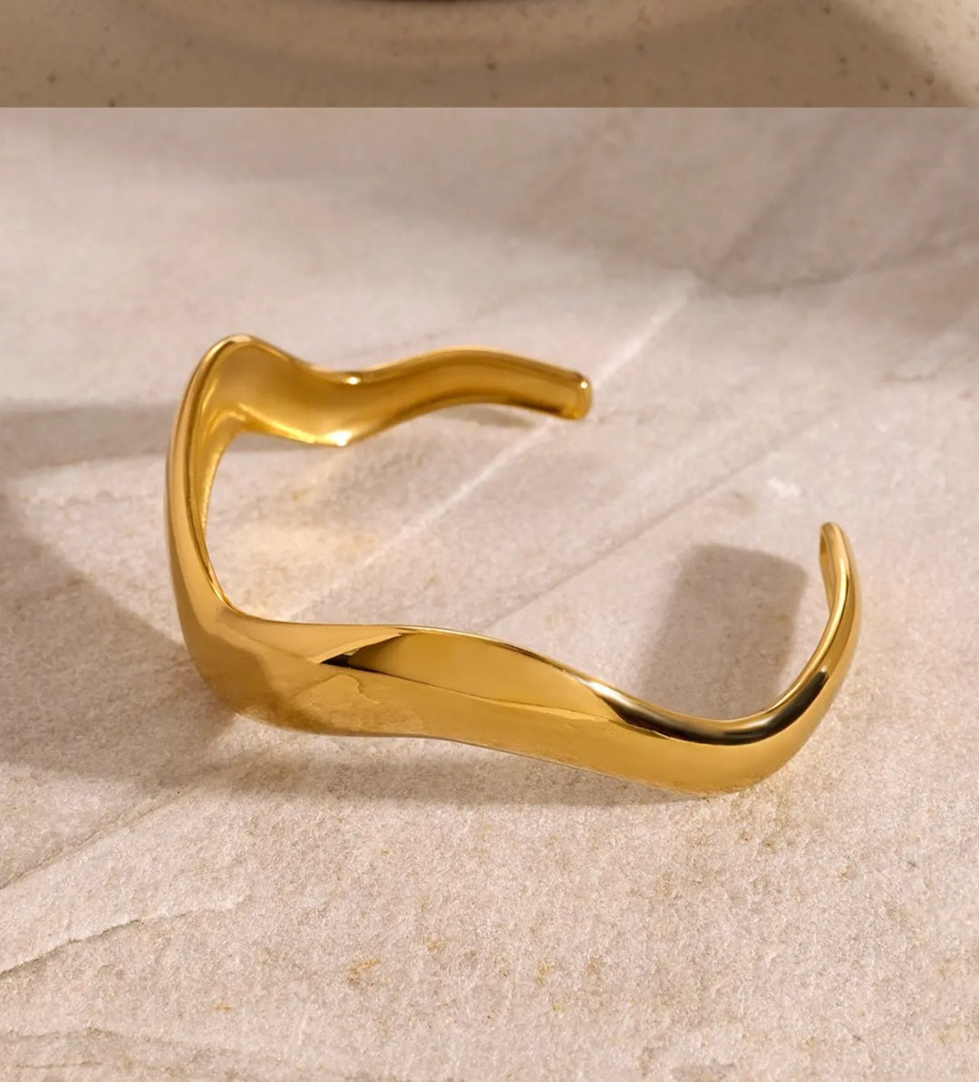 18K PVD Gold statement open cuff on a textured beige surface