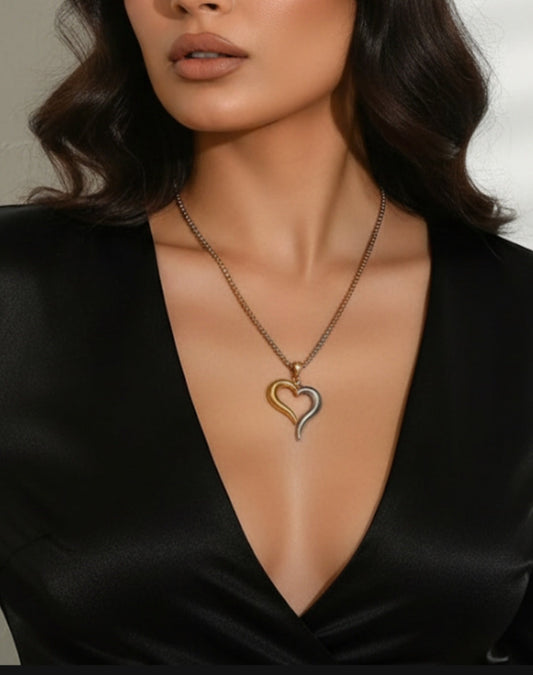Woman wearing a gold heart-shaped necklace against a neutral Mixed Metal Heart Necklace featuring a large, open 18K gold-plated heart pendant on a unique square stainless steel chain.background