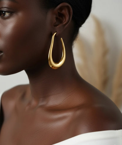 Close-up of a person wearing a gold hoop earring with a neutral background