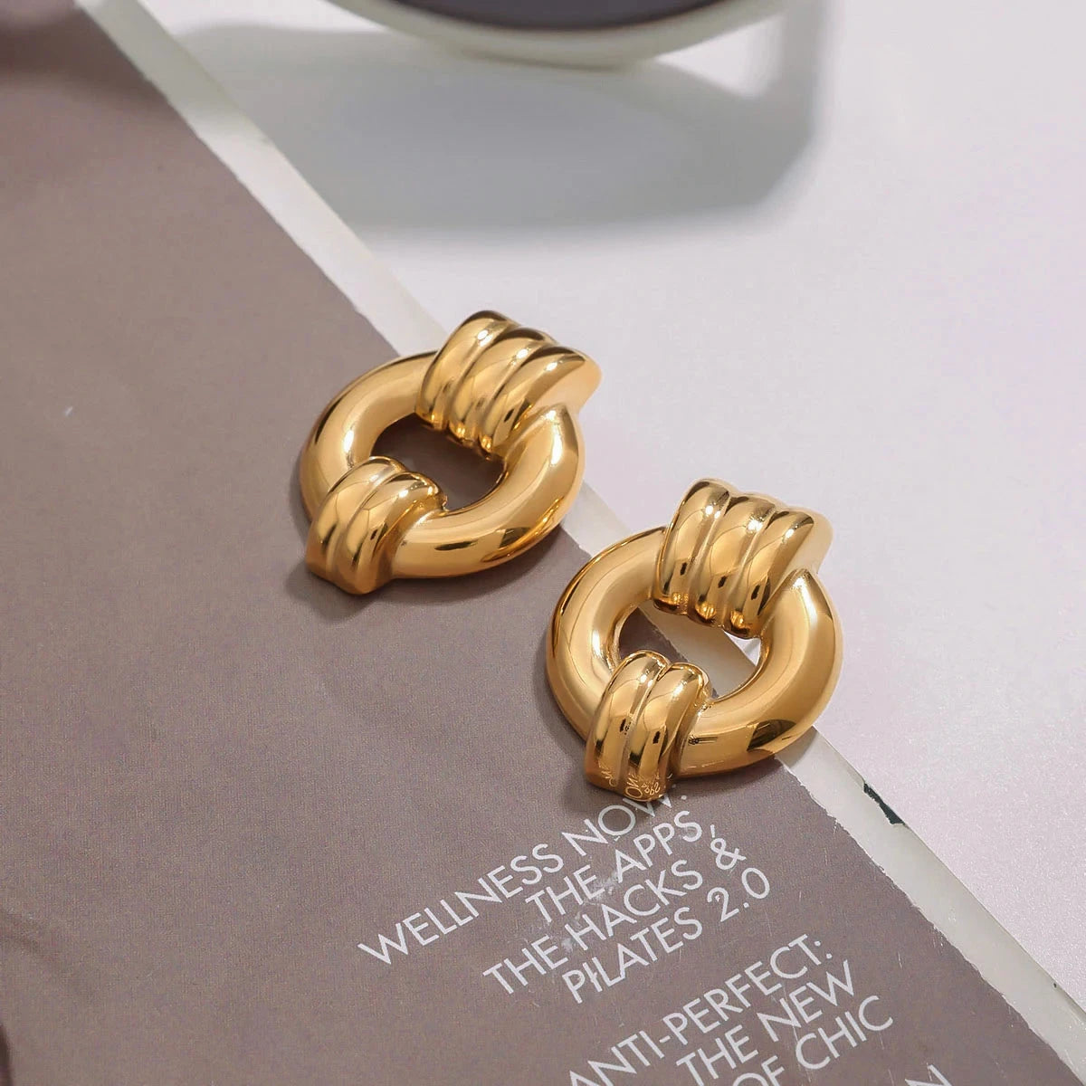 18K PVD gold hoop earrings on a magazine with text