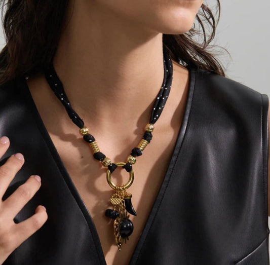 Person wearing a black and gold heart charm necklace with a plain background