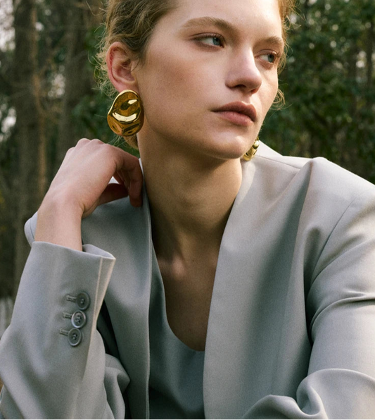 Woman wearing gold earrings outdoors with trees in the background