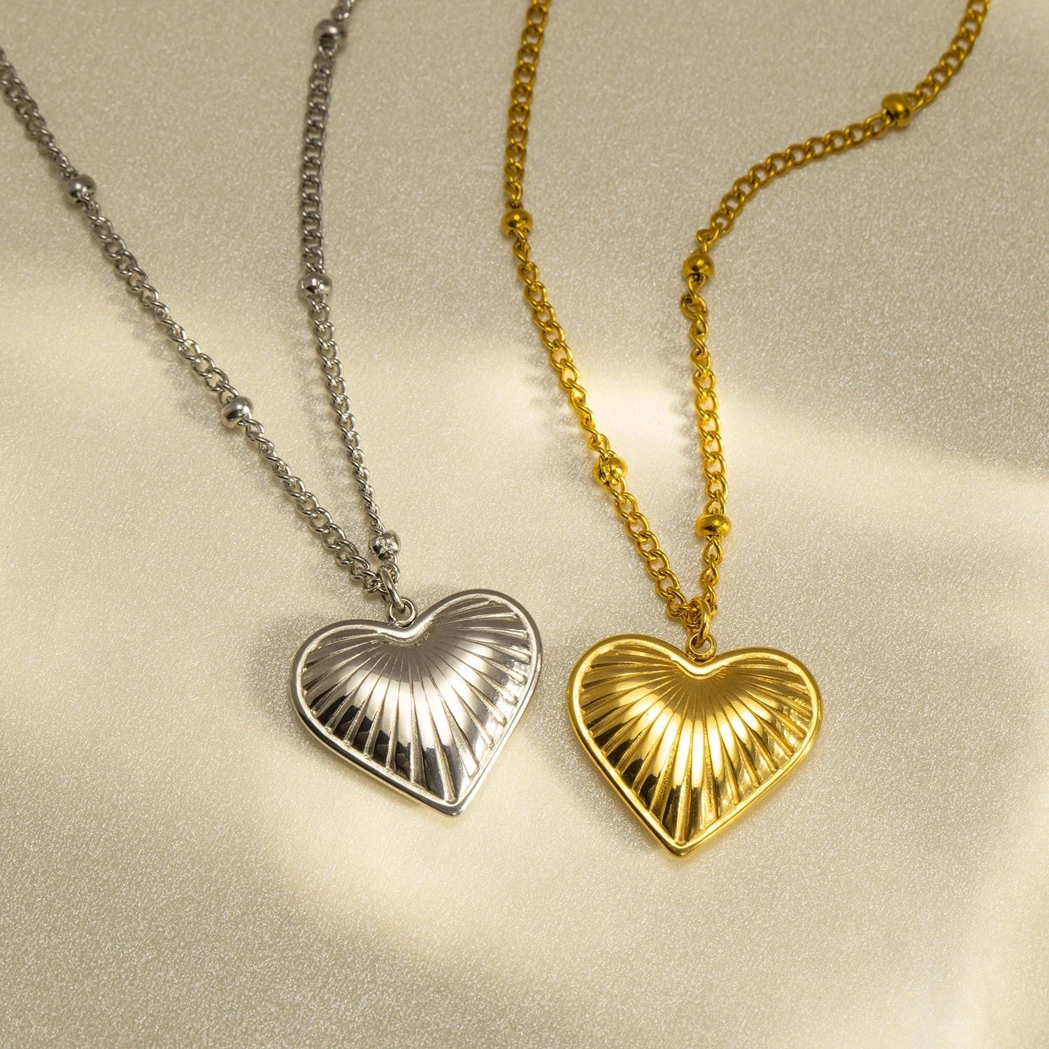 Two heart-shaped pendants on chains, one gold and one silver, on a light background.