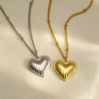 Two heart-shaped pendants on chains, one gold and one silver, on a light background.