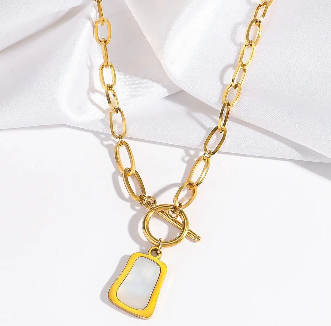 Close-up of the Zena Necklace pendant, highlighting the shimmer of the pearl oyster charm next to the geometric trapezoid.